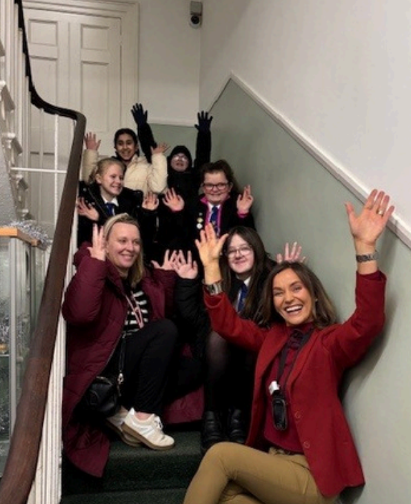 Woman who runs the deaf centre (2024) sitting on staircase smiling with volunteer group.