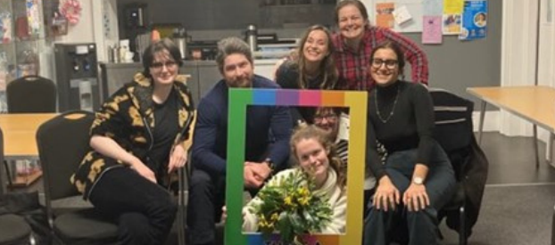 People sitting together in a group. One person has their face in a rainbow frame.