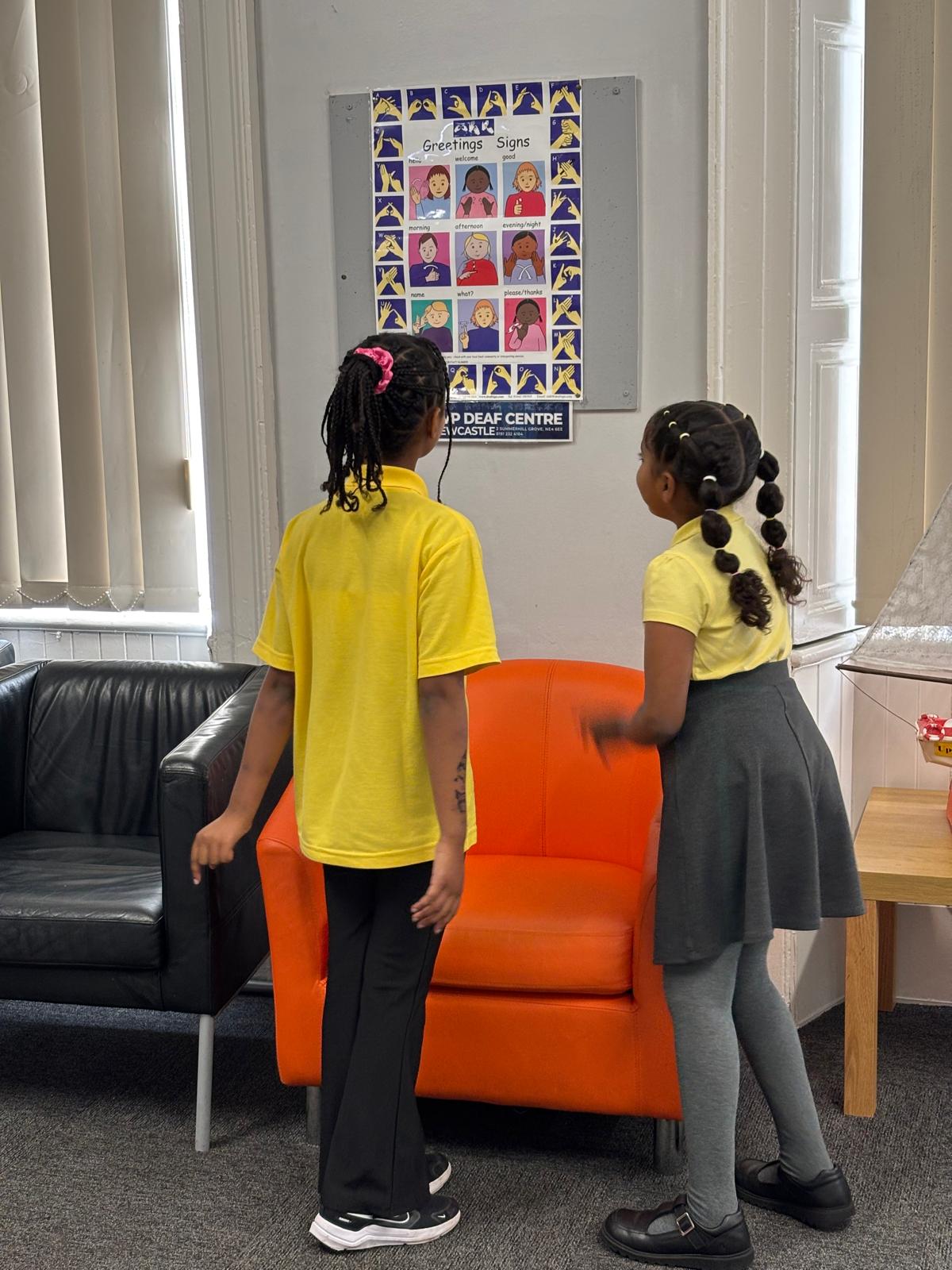 Two children looking at a sign language chart.