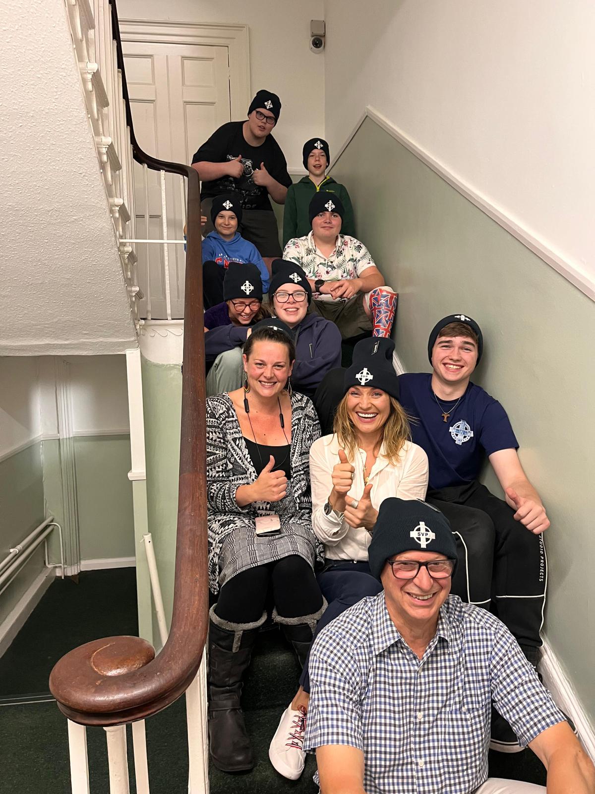 Woman who runs the deaf centre (2024) sitting on staircase smiling with volunteer group.