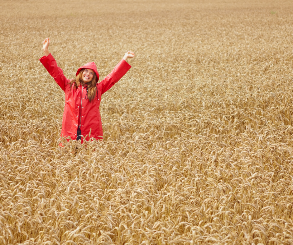 woman waving in red raincoat in a field of wheat