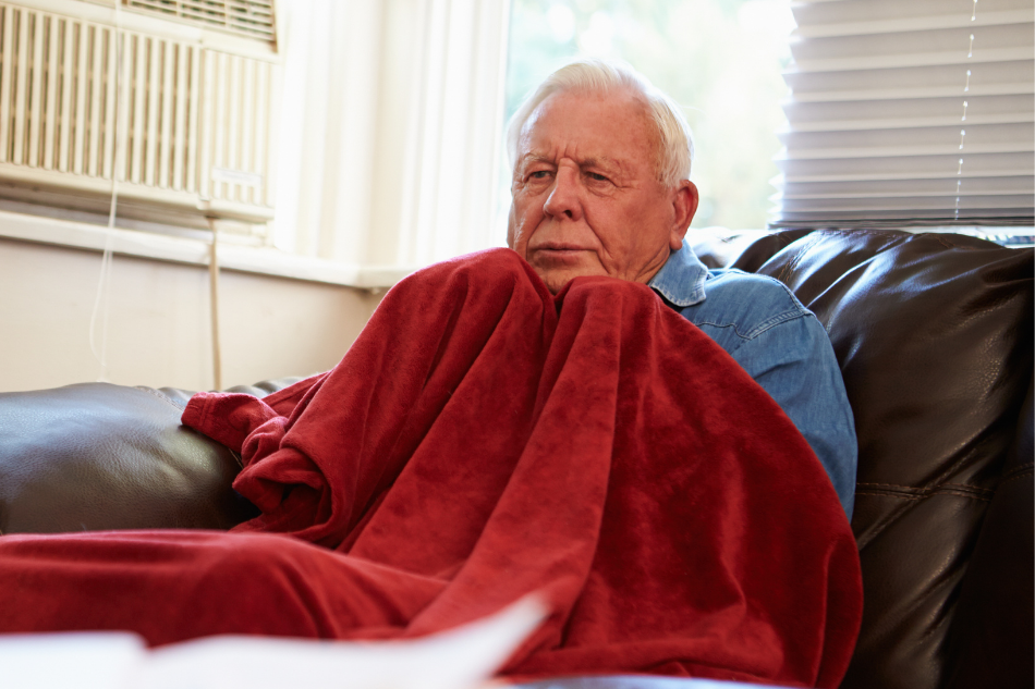 Elderly man freezing in the living room and pulling red blanket tight to him
