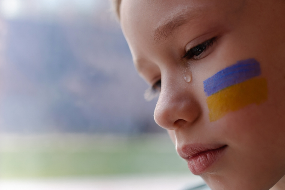Ukrainian child with flag of Ukraine on cheek, crying on a bus