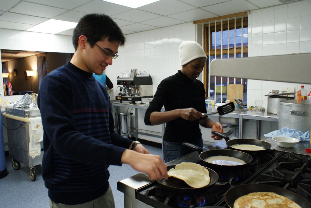 Asian boy and black girl making pancakes in industrial kitchen.